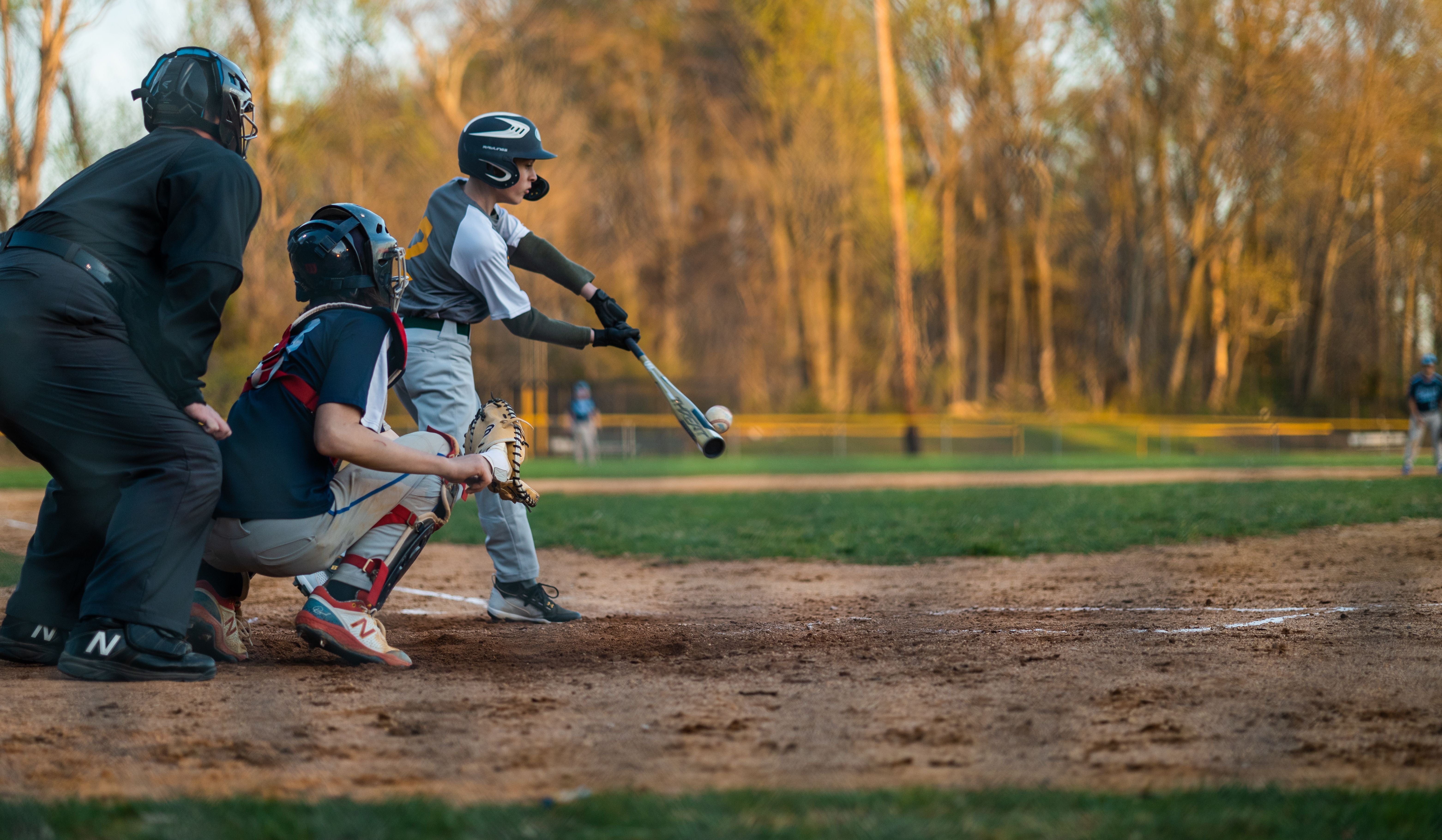 Youth baseball batter connecting with the ball at home plate in golden evening light